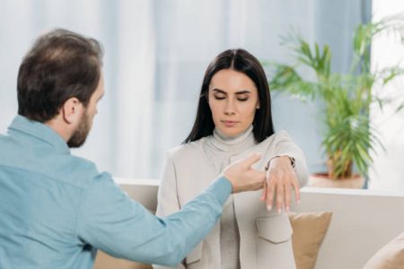 bearded hypnotist holding wrist of young woman with closed eyes during hypnotherapy