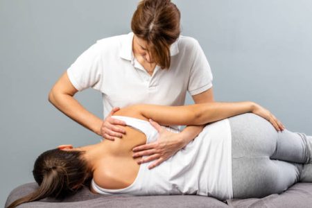 Close up of female osteopath doing shoulder blade therapy on young woman.